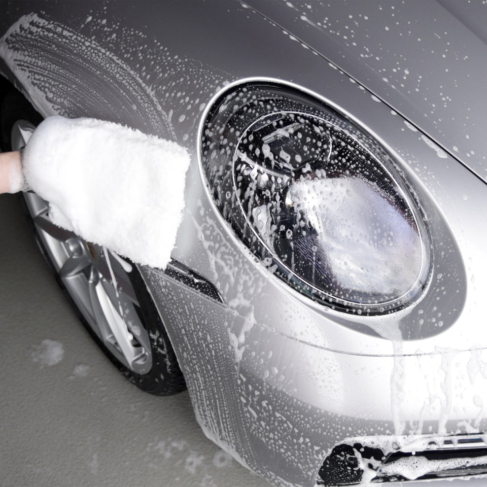 Waschhandschuh mit Autoshampoo-Schaum am Scheinwerfer eines silbernen Porsche 911