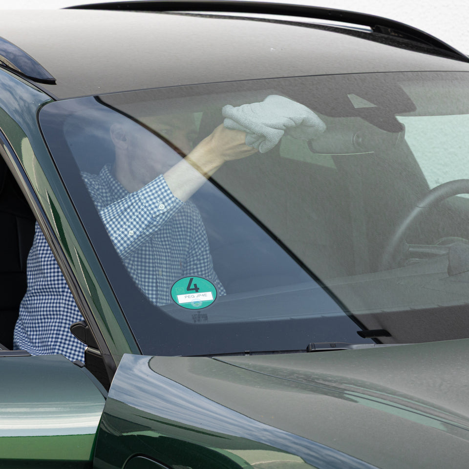 Mann im Fahrzeug reinigt den oberen Rand der Windschutzscheibe am Innenspiegel mit einem Mikrofasertuch
