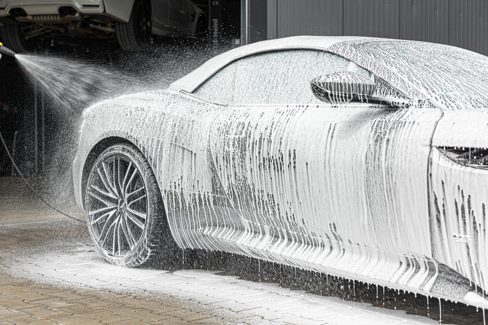 Aston Martin Cabriolet unter dichtem Snow-Foam-Schaum, im Hintergrund die Schaumlanze