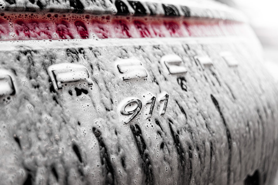 Autoshampoo-Schaum auf dem Heck eines schwarzen Porsche 911, Nahaufnahme am 911-Schriftzug