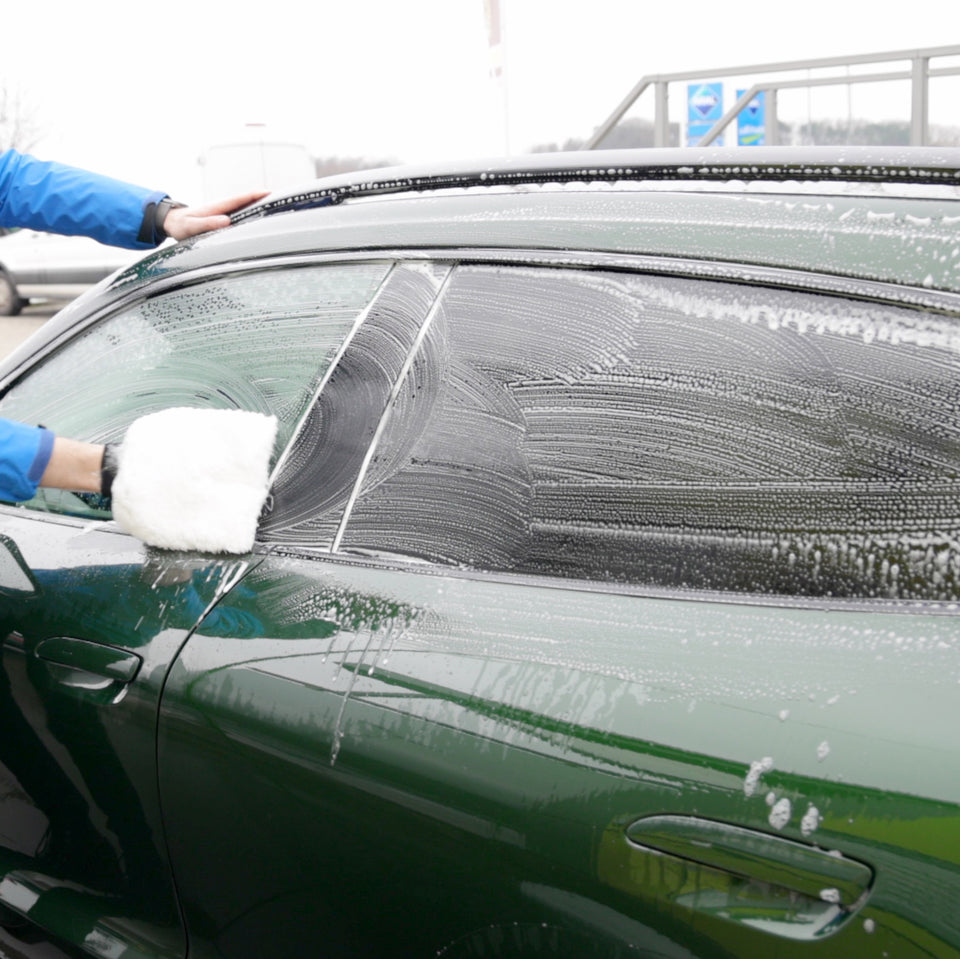 Waschhandschuh mit Autoshampoo am Seitenfenster eines dunkelgrünen Porsche Taycan Cross Turismo