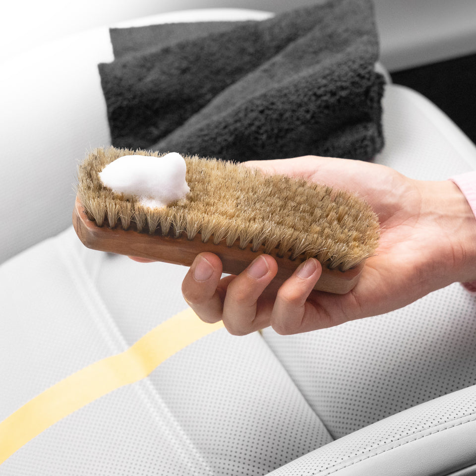 Lederreiniger-Schaum auf der KULT Rosshaarbürste über einem hellen, teilweise abgeklebten Ledersitz