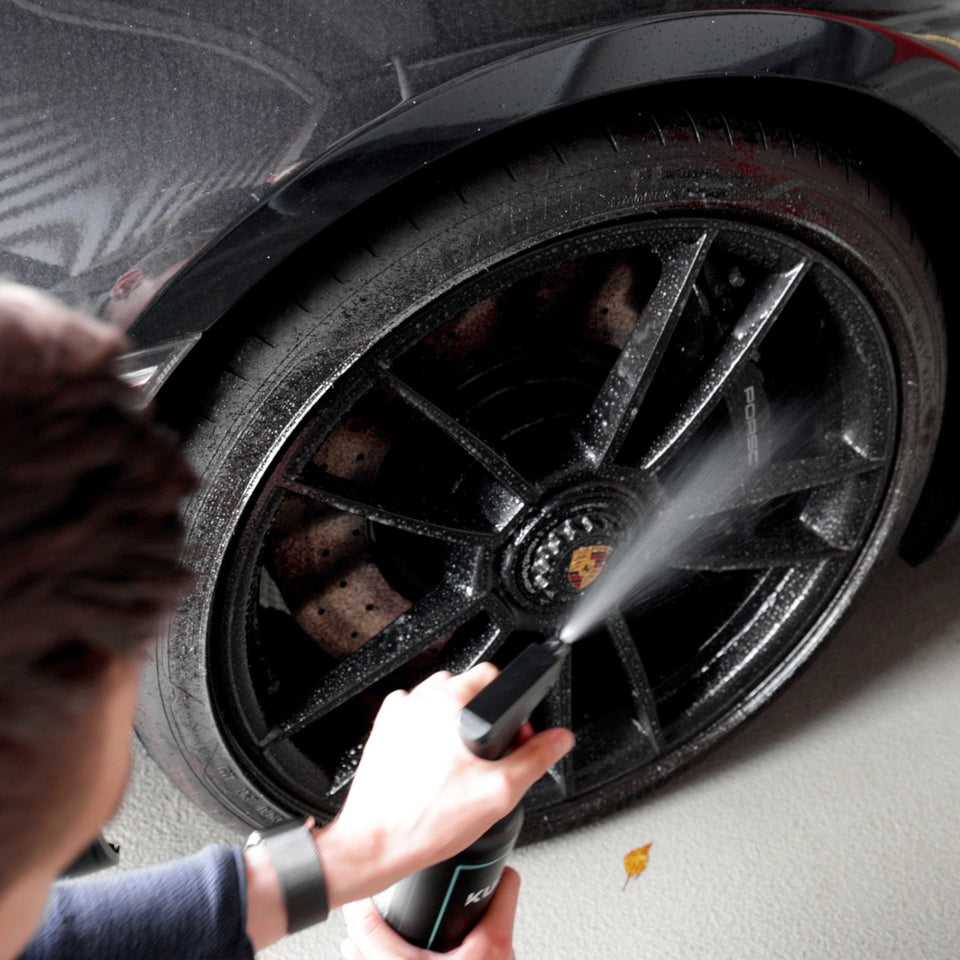 Felgenreiniger wird auf eine schwarze Porsche-Felge gesprüht