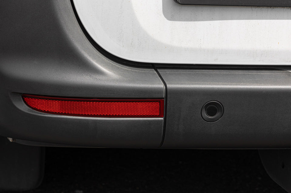 Unlackierter Kunststoff-Stoßfänger mit Reflektor und Parksensor, die Oberfläche wirkt grau und matt