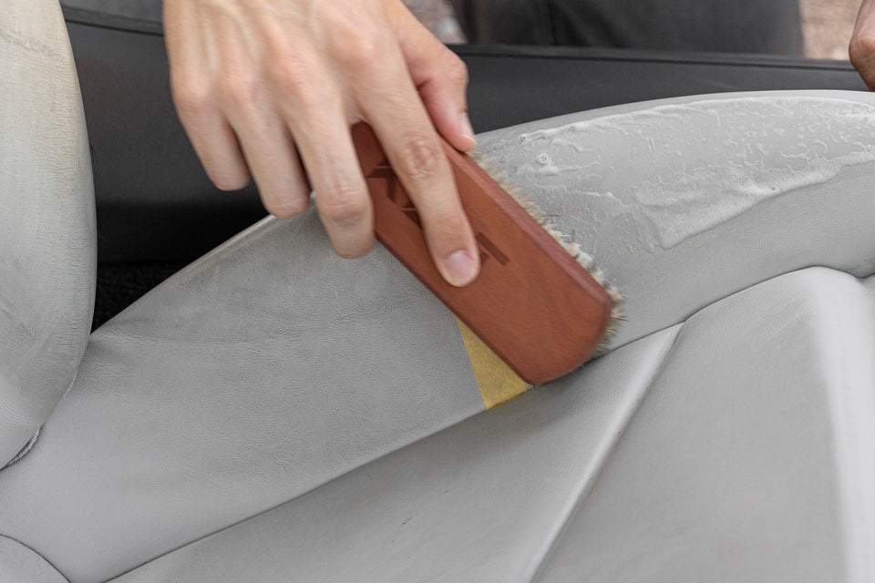 Die KULT Rosshaarbürste arbeitet Lederreiniger-Schaum mit wenig Druck in eine helle Ledersitzwange ein