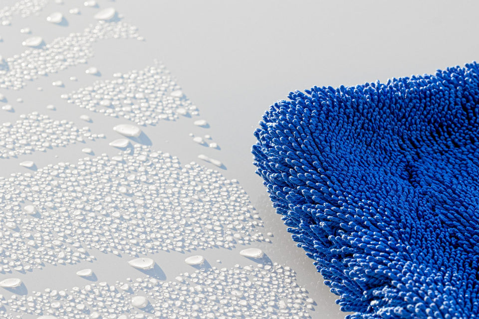 Nahaufnahme: Fasern des blauen Trockentuchs neben Wassertropfen auf hellem Lack