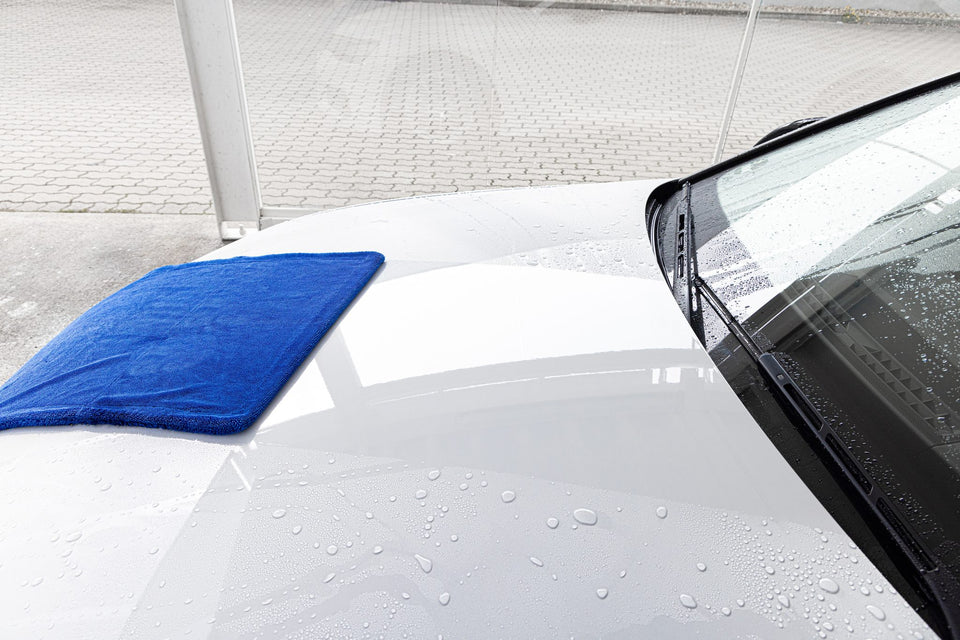 Blaues Trockentuch auf der nassen Motorhaube eines weißen Autos