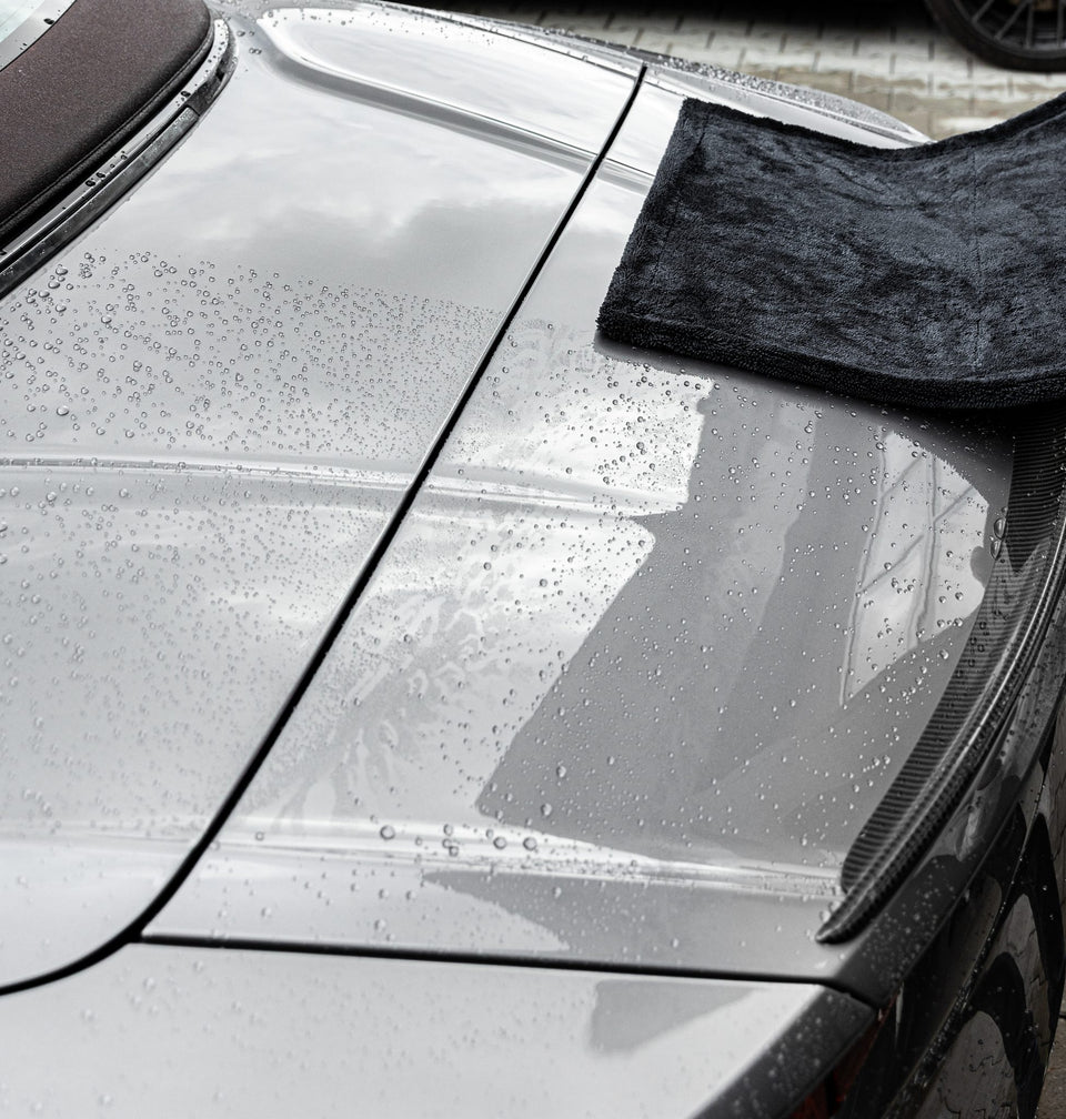 Schwarzes Trockentuch auf dem nassen hinteren Seitenteil eines silbergrauen Autos