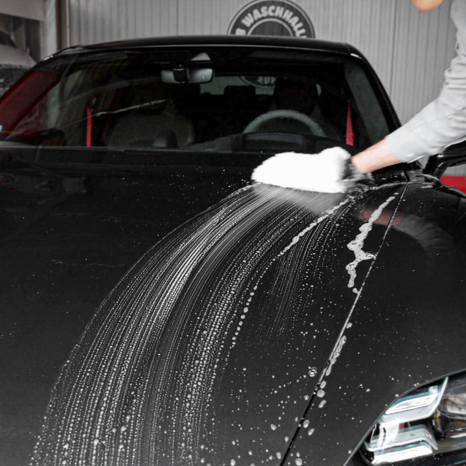 Waschhandschuh gleitet mit Schaum über die schwarze Tür eines Porsche Taycan GTS