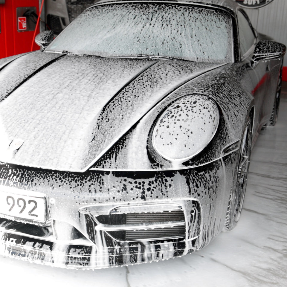 Schwarzer Porsche 911 in der Waschbox, bedeckt mit dichtem Schaum