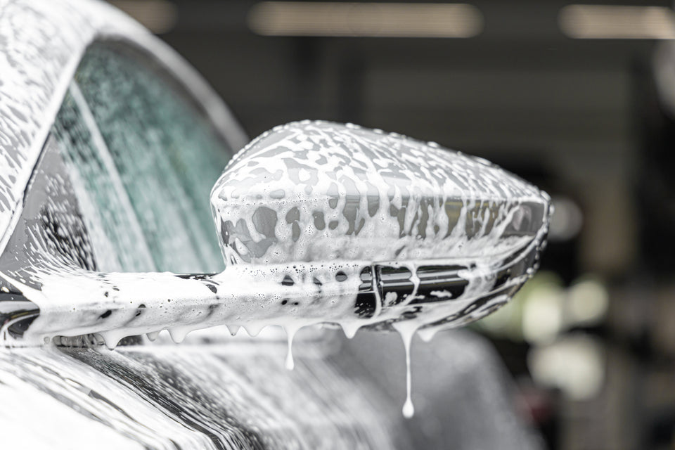 Autoshampoo-Schaum mit Tropfen am Seitenspiegel eines grauen Aston Martin