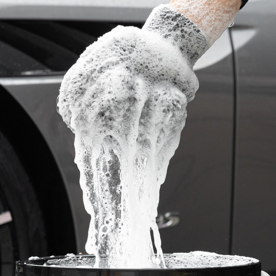 Waschhandschuh voller Autoshampoo-Schaum über dem Eimer