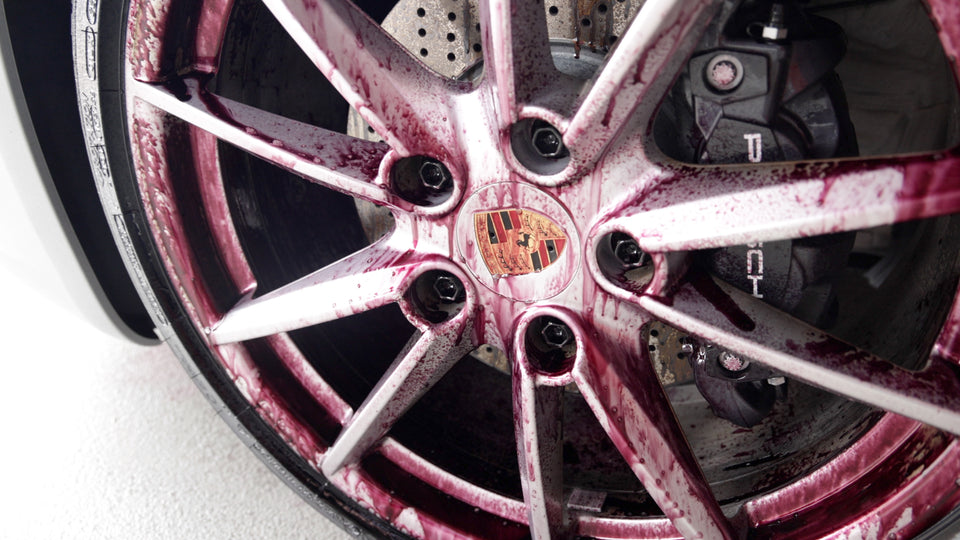 Silberne Porsche-Felge vor gelochter Bremsscheibe, der Felgenreiniger färbt sich violett