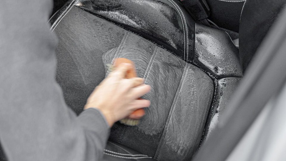 Sitzmittelbahn eines Autositzes wird mit Innenraumreiniger und Rosshaarbürste eingeschäumt