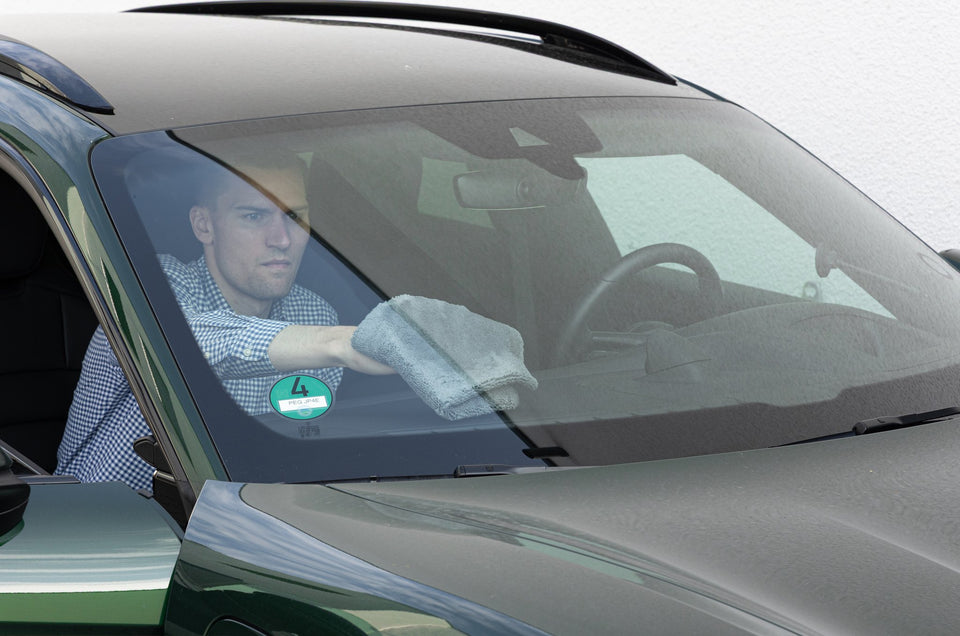 Mann im Fahrzeug wischt die Windschutzscheibe von innen mit einem grauen Mikrofasertuch
