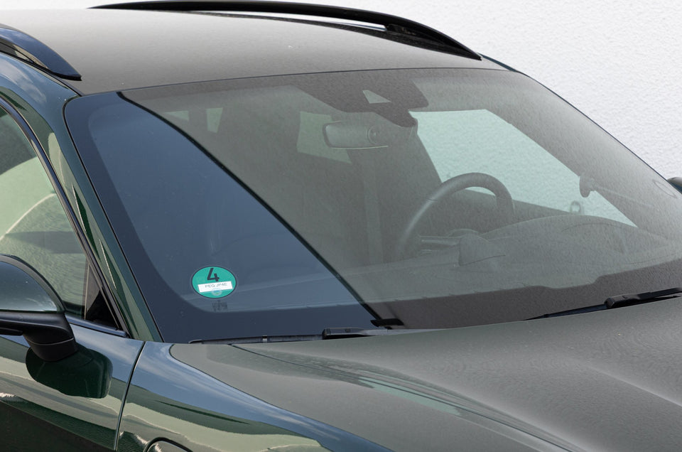 Windschutzscheibe eines dunkelgrünen Fahrzeugs vor der Reinigung, feine Schmutzpunkte und Tropfen auf dem Glas