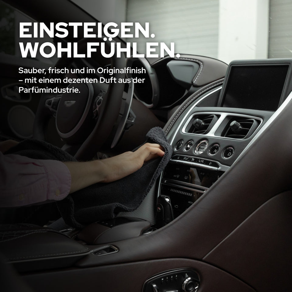 Mittelkonsole und Cockpit in dunklem Leder und Kunststoff, ein Mikrofasertuch wischt über eine Fläche