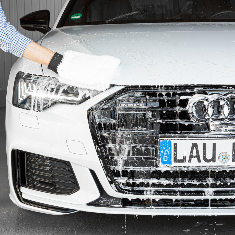 Kühlergrill eines weißen Audi A6 wird mit Waschhandschuh und Autoshampoo nachgewaschen