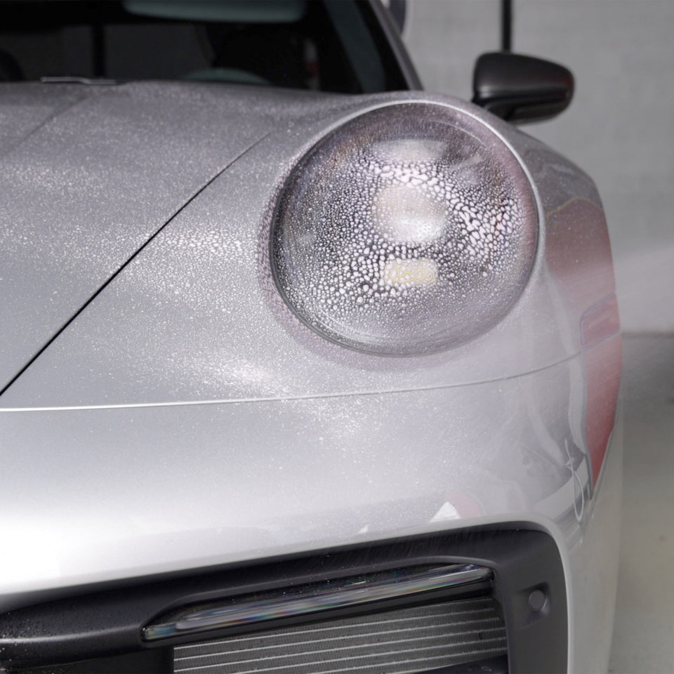 Insektenentferner wirkt auf Scheinwerfer und Front eines silbernen Porsche 911 ein